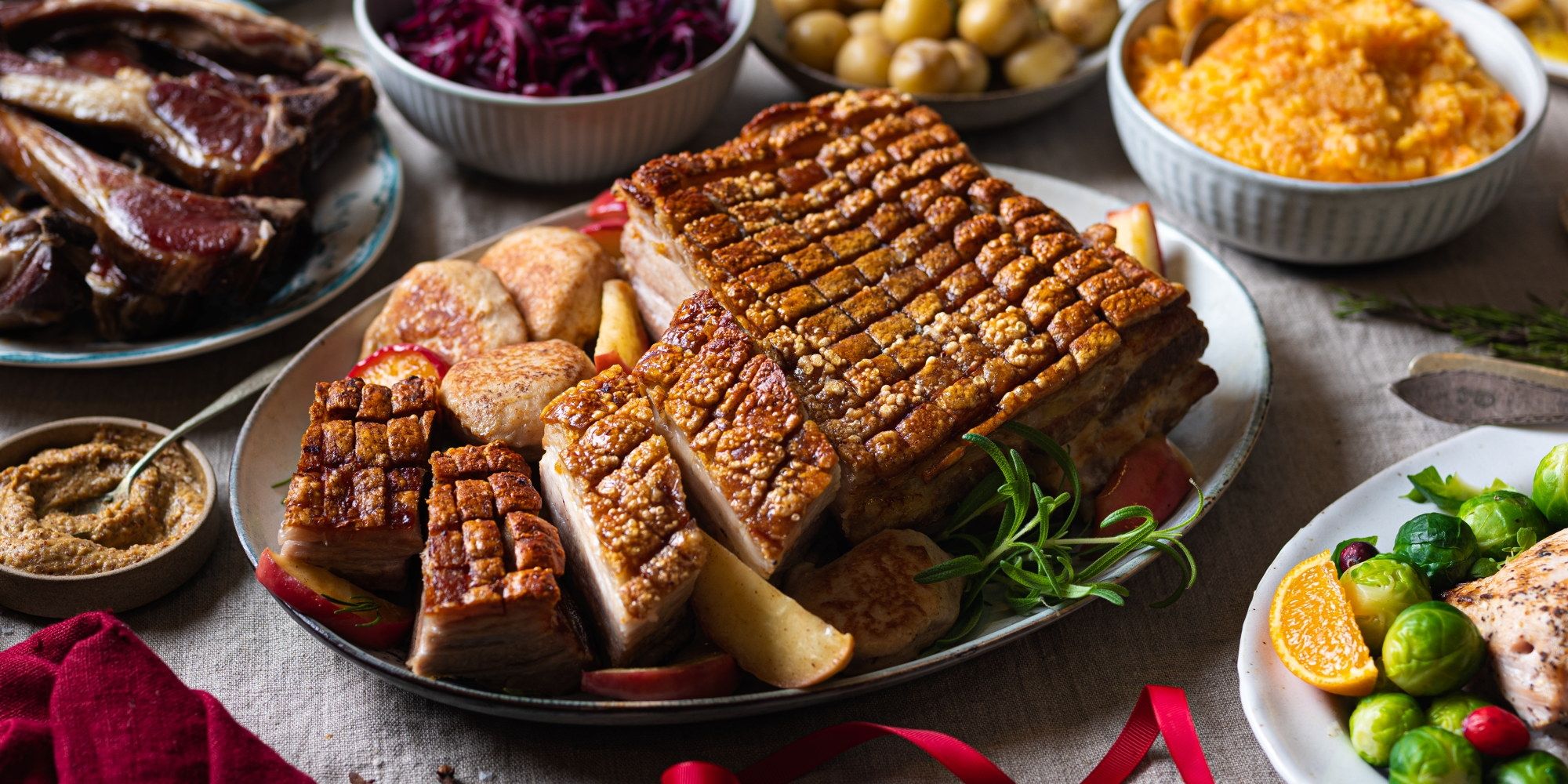 Et julebord med ribbe, medisterkaker og tilbehør som rosenkål og appelsin, omgitt av ulike retter og garnityr.