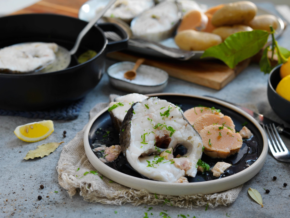 Skreimølje med kokt skrei, tilbehør som sitron, rømme og grønnsaker på et fat og bord.