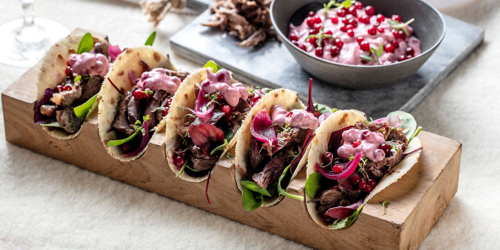 Fire tacos fylt med kjøtt, grønnsaker og rød løk, med en bolle med salsa ved siden av, på et bord.