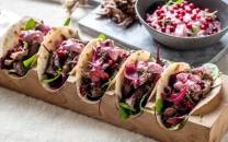 Fire tacos fylt med kjøtt, grønnsaker og rød løk, med en bolle med salsa ved siden av, på et bord.