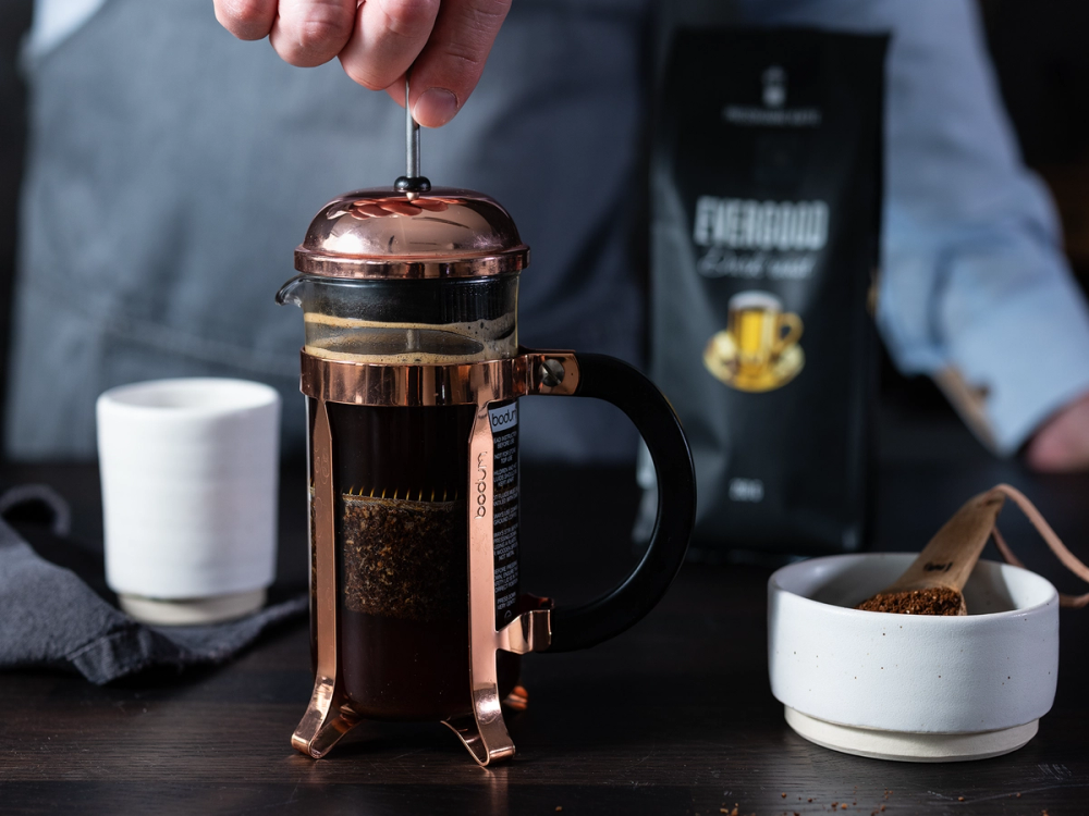 En person lager kaffe med en presskanne, mens en kopp står klar ved siden av.
