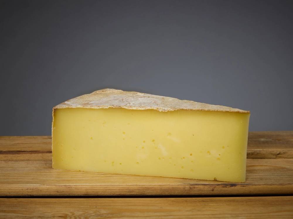 Et stykke gul ost på et trebrett mot en grå bakgrunn