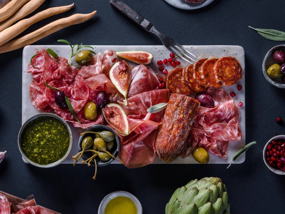 Spekemat med ulike typer kjøtt, oliven, fiken og urter på et serveringsfat.