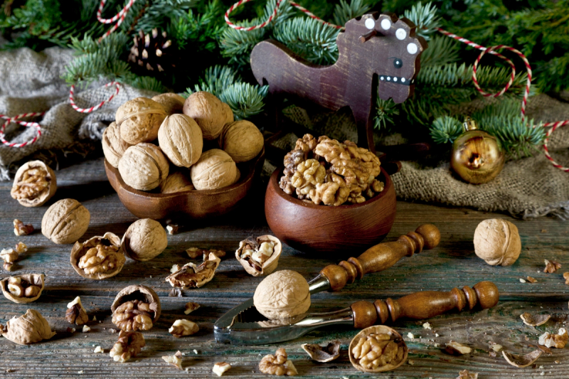 Valnøtter og julepynt på et bord med granbar og dekorasjoner, som antyder en juledekorasjon.