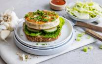 Fiskeburger med stekt fisk, salat og dressing på en tallerken, med en skål med ketchup og en skål med kål i bakgrunnen.