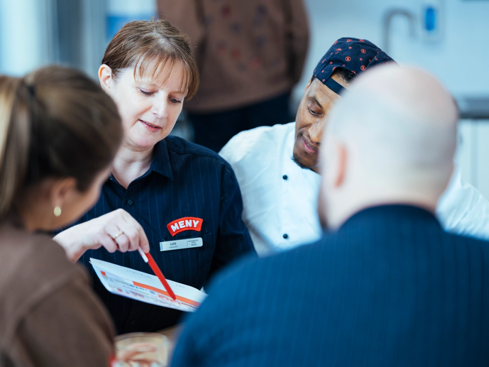 En gruppe ansatte som snakker og samarbeider rundt et bord på et kontor eller møteplass.