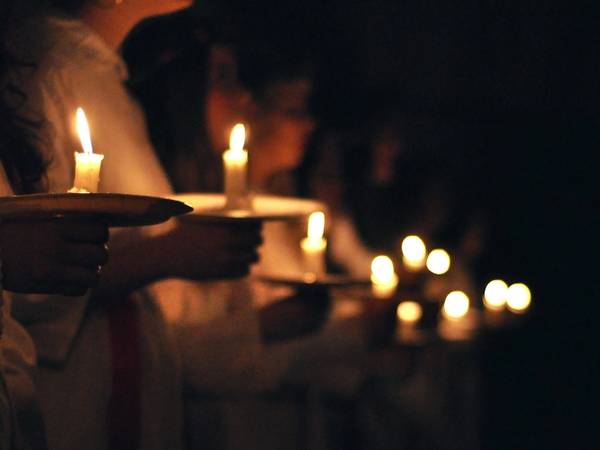Personer som holder lysende lyslykter under en mørk kveld, sannsynligvis under en lucia-feiring.