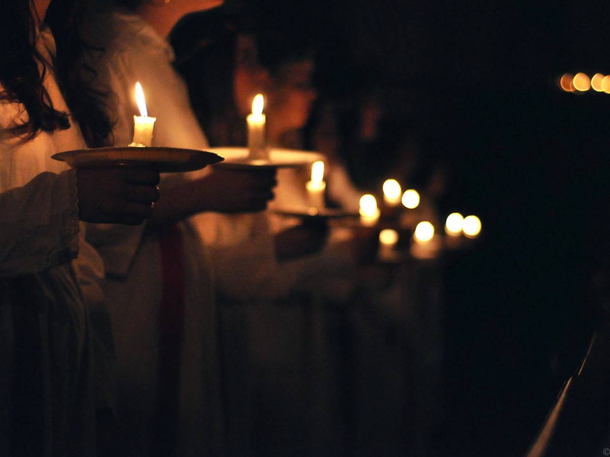 Personer som holder lysende lyslykter under en mørk kveld, sannsynligvis under en lucia-feiring.