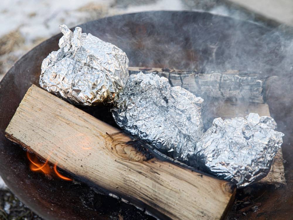 Bakt potet pakket inn i aluminiumsfolie på en grill med glødende kull under.