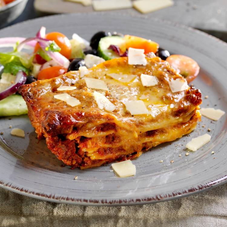 En porsjon takeaway lasagne med ost og salat på en tallerken.