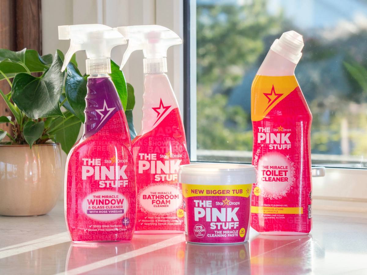 Fire rengjøringsprodukter fra The Pink Stuff-serien plassert på et kjøkkenbenk med vindu i bakgrunnen.