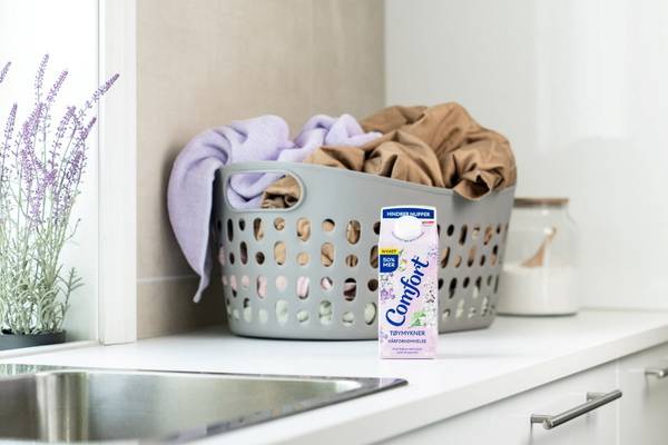 En vaskekurv med klesvask og en melkekartong med Comfort på en kjøkkenbenk