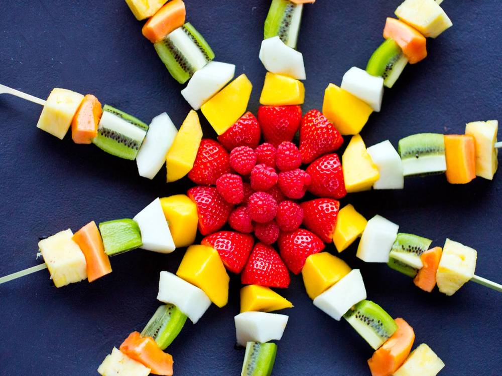 Fargerike fruktspyd med biter av kiwi, melon, ananas og jordbær på en mørk bakgrunn