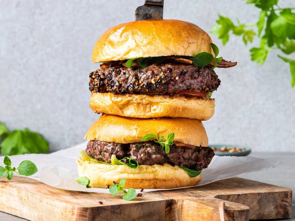 En stor burger med bacon, kjøttboller, salat og brød, stablet høyt på en skjærefjøl.