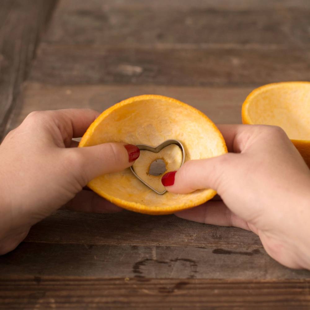 Hender som skjærer ut en hjerteformet bit av en klementin med en kniv på et trebord.