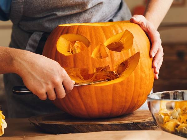 En person skuler ut innmaten av en gresskar for å lage en halloween-dekorasjon, med en bolle med gresskarbiter ved siden av.