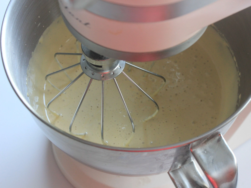 En kjøkkenmaskin som pisker en gul væske i en bolle, sannsynligvis egge- eller kremblanding.