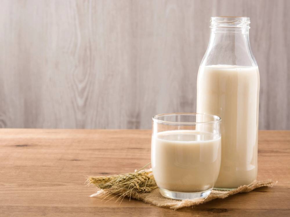 Et glass og en flaske med havremelk står på et bord med en liten haug med havre ved siden av.