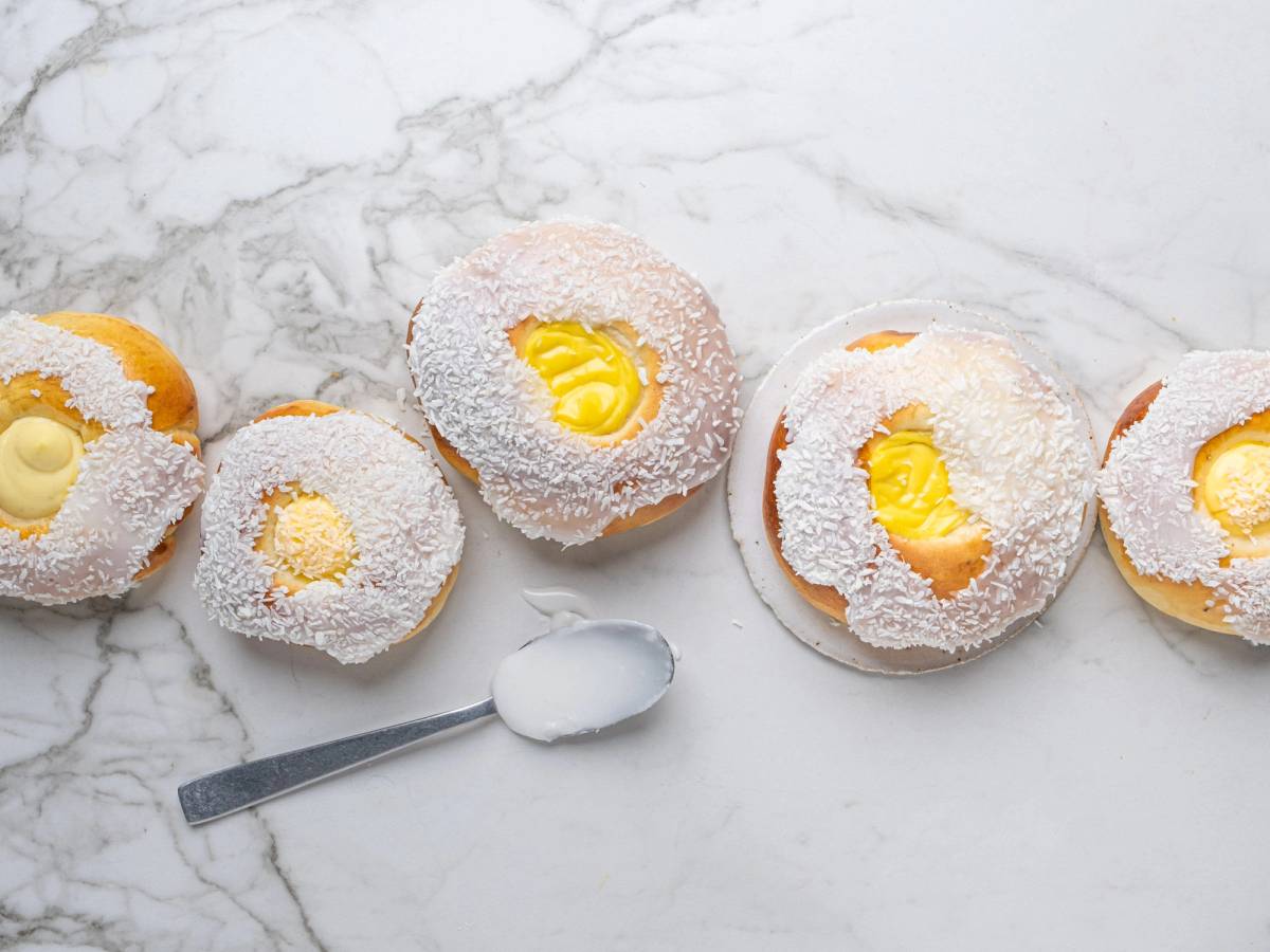 Boller med skolebrød-fyll og kokos på toppen, lagt ut på en hvit marmorgulv, med en liten skje ved siden av.