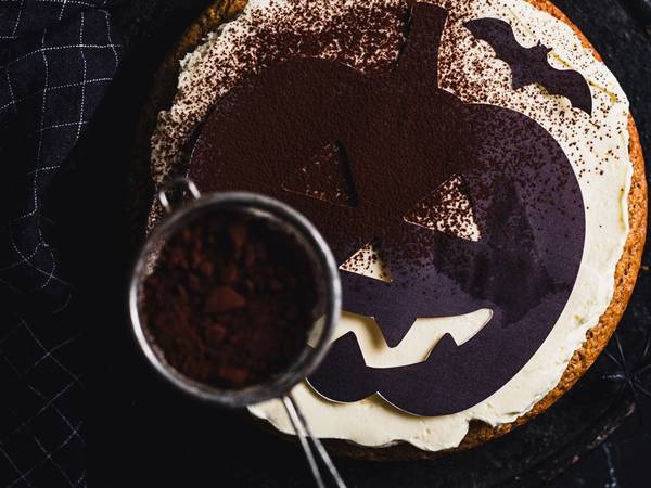 En Halloween-kake med et gresskaransikt som blir dekorert med melis, sett ovenfra.