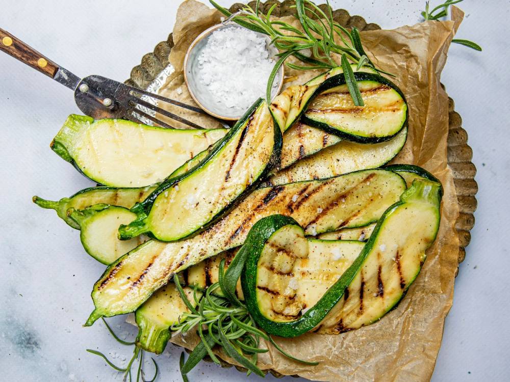 Grillet squash med grillmerker, servert med en skje med dip og fersk rosmarin på et papirunderlag.