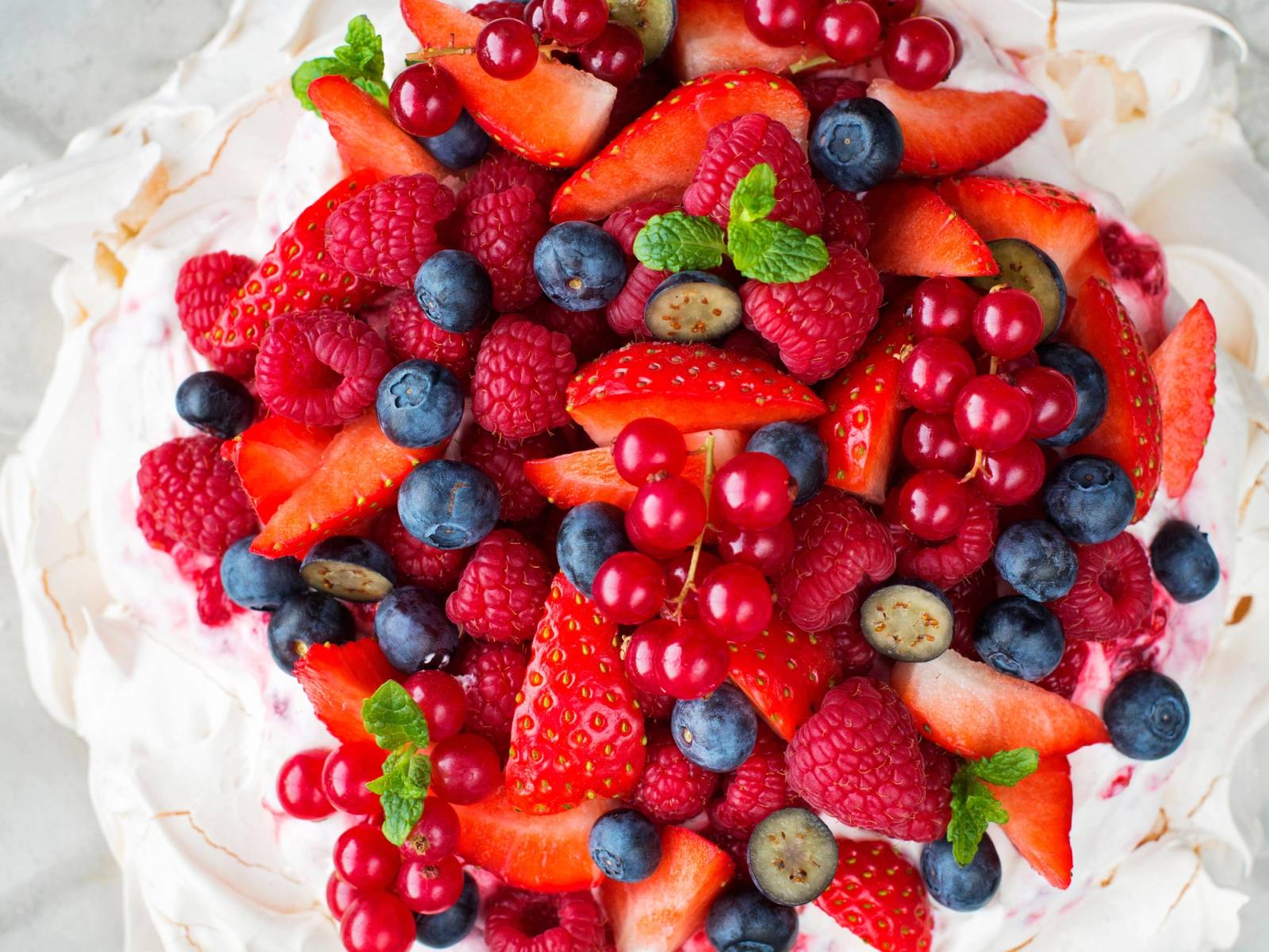 En kake dekket med et utvalg av friske bær som jordbær, bringebær, blåbær og rips, pyntet med mynteblader.