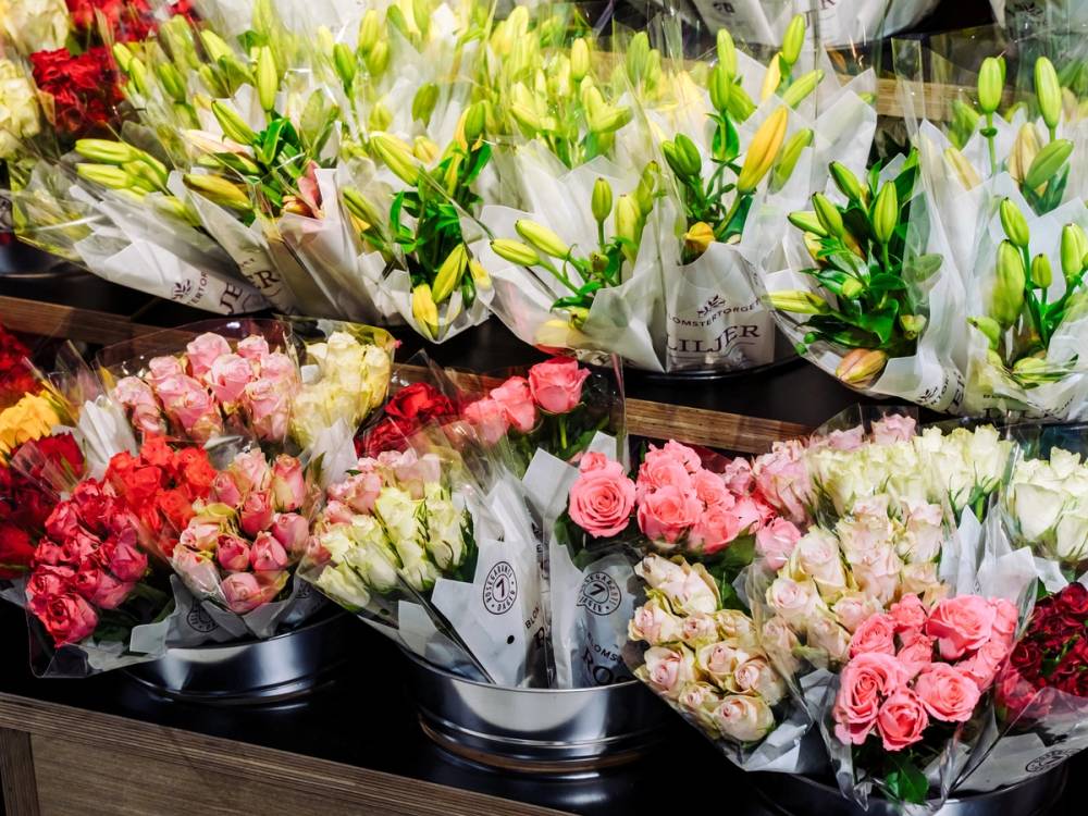 Fargerike blomsterbuketter i en blomsterbutikk, med rosa og hvite blomster, og grønne blader, på en butikkhylle.