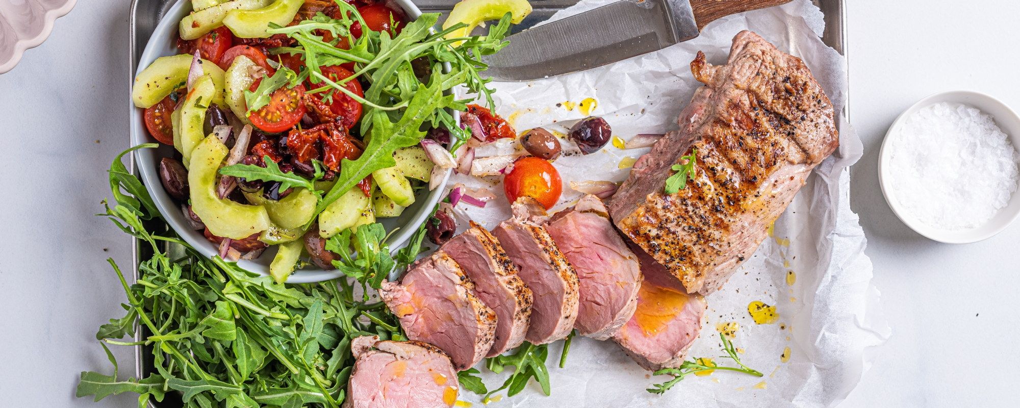 Svinefilet servert med tatziki og en frisk salat med grønnsaker og tomater, på et hvitt fat.