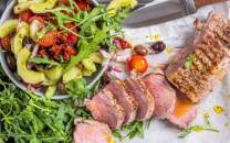 Svinefilet servert med tatziki og en frisk salat med grønnsaker og tomater, på et hvitt fat.