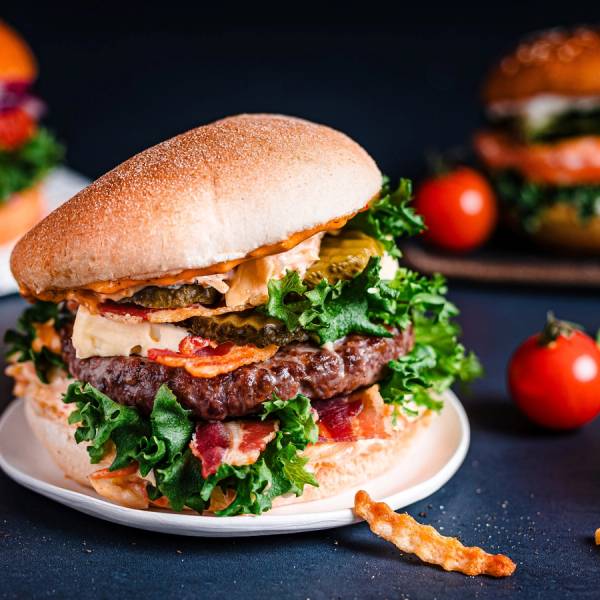 En saftig burger med salat, kjøttkake og brød, plassert på en hvit tallerken med noen cherrytomater rundt.