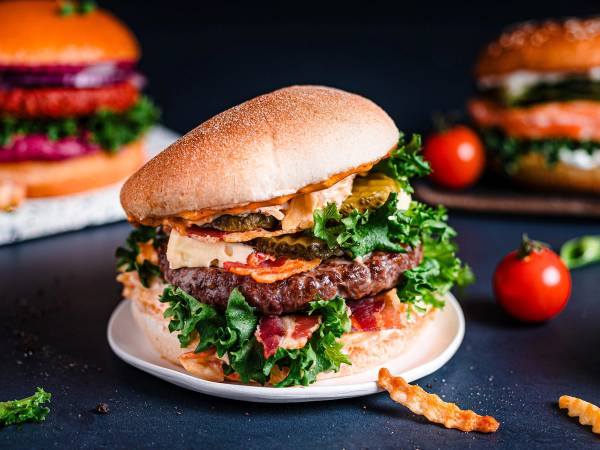En saftig burger med salat, kjøttkake og brød, plassert på en hvit tallerken med noen cherrytomater rundt.