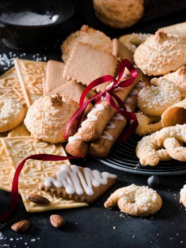 Et utvalg julekaker, inkludert kjeks, småkaker og en kjeks med hvit glasur, pyntet med en rød sløyfe, på en svart tallerken.