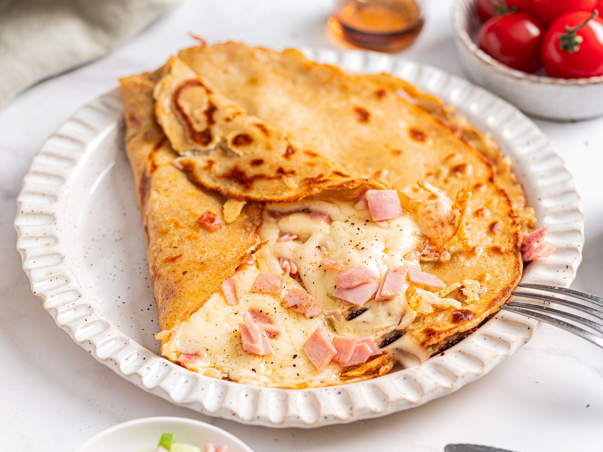 Pannekake fylt med ost og skinke på en hvit tallerken med en skje ved siden av.