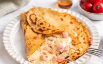 Pannekake fylt med ost og skinke på en hvit tallerken med en skje ved siden av.