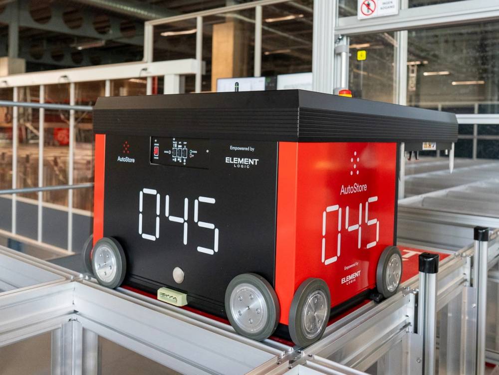 En robot med en digital skjerm som viser klokken 04:45, plassert på en metallramme i et industriområde.