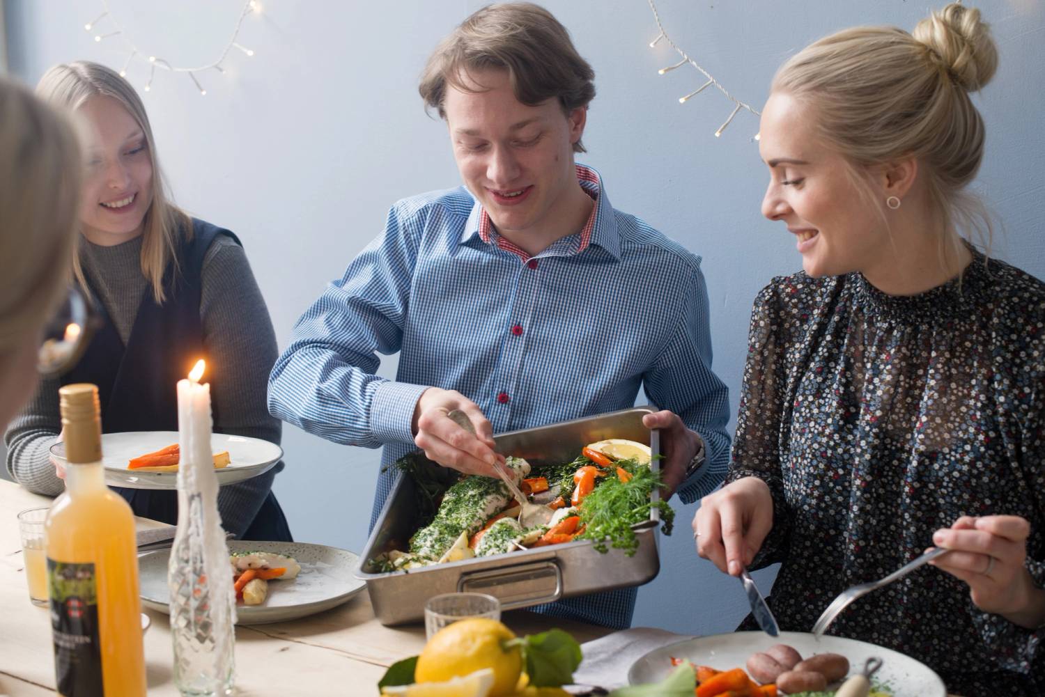 Personer som spiser og har en fiskefest med ulike retter på bordet, inkludert en stor fisk på tallerkenen.