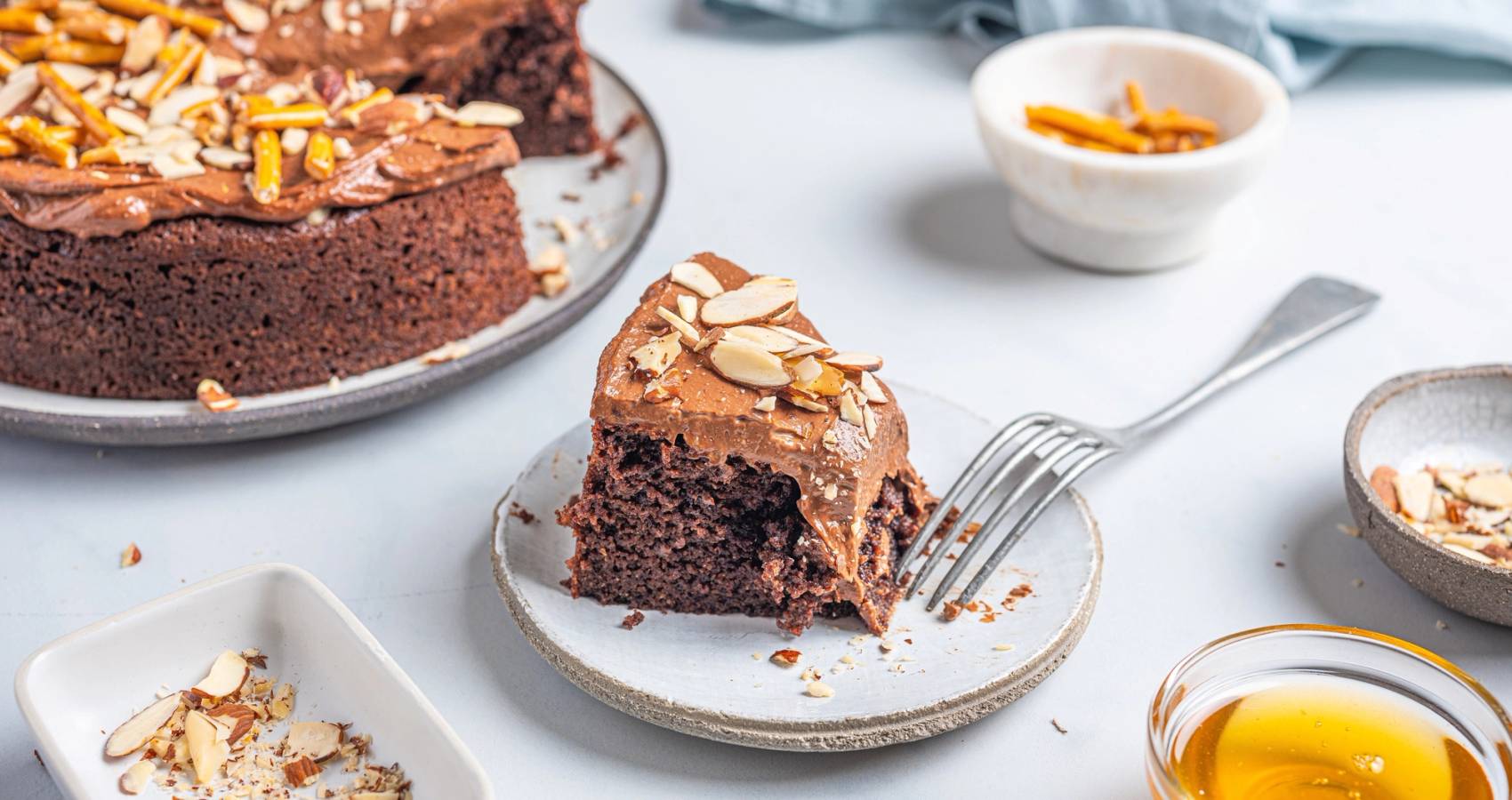 Et stykke sjokoladekake uten melk og mel på en liten tallerken, med en gaffel ved siden av, omgitt av små skåler med tilbehør.