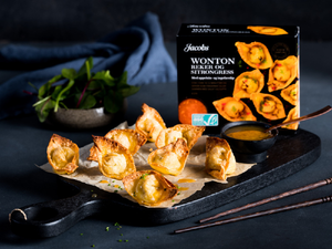 Friterte wonton med en boks med ju wonton og en liten skål med saus ved siden av, på en svart steinplate.