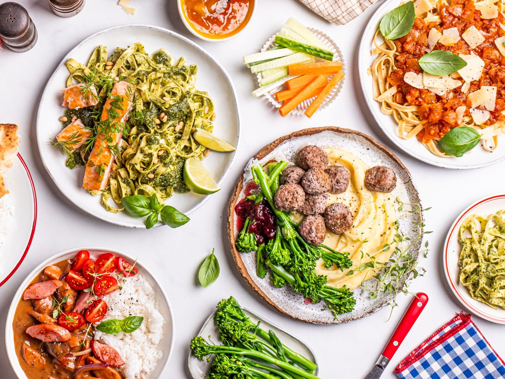 Et utvalg av middagsretter inkludert pasta med kjøttboller, salat, pizza og grønnsaker på bordet.