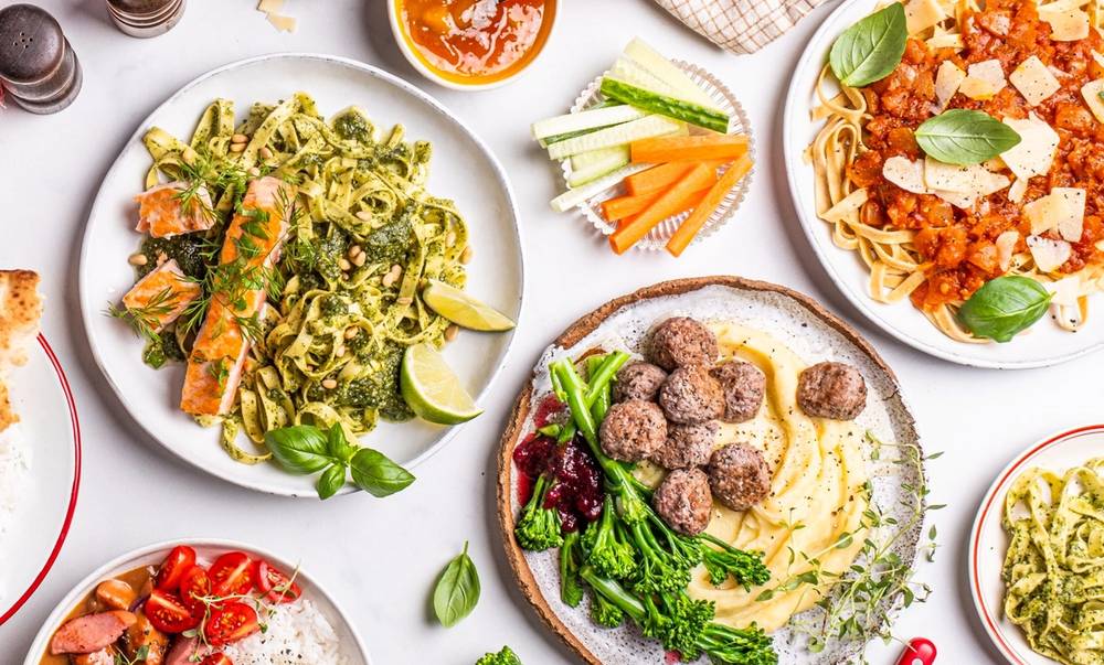 Et utvalg av middagsretter inkludert pasta med kjøttboller, salat, pizza og grønnsaker på bordet.