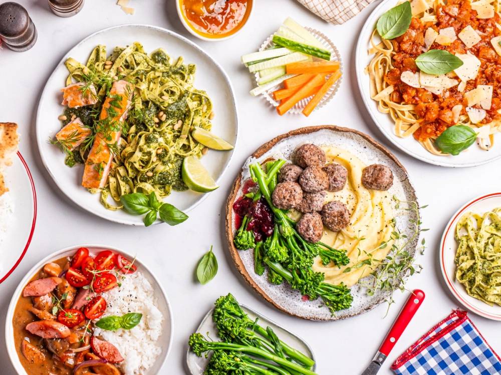 Et utvalg av middagsretter inkludert pasta med kjøttboller, salat, pizza og grønnsaker på bordet.