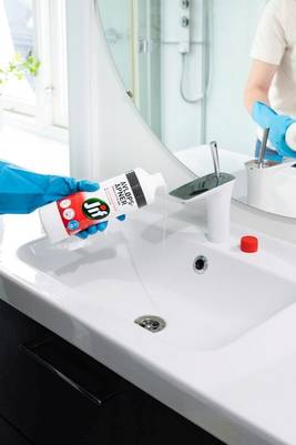En person med blå hansker heller Jif avløpsåpner i vasken på badet.