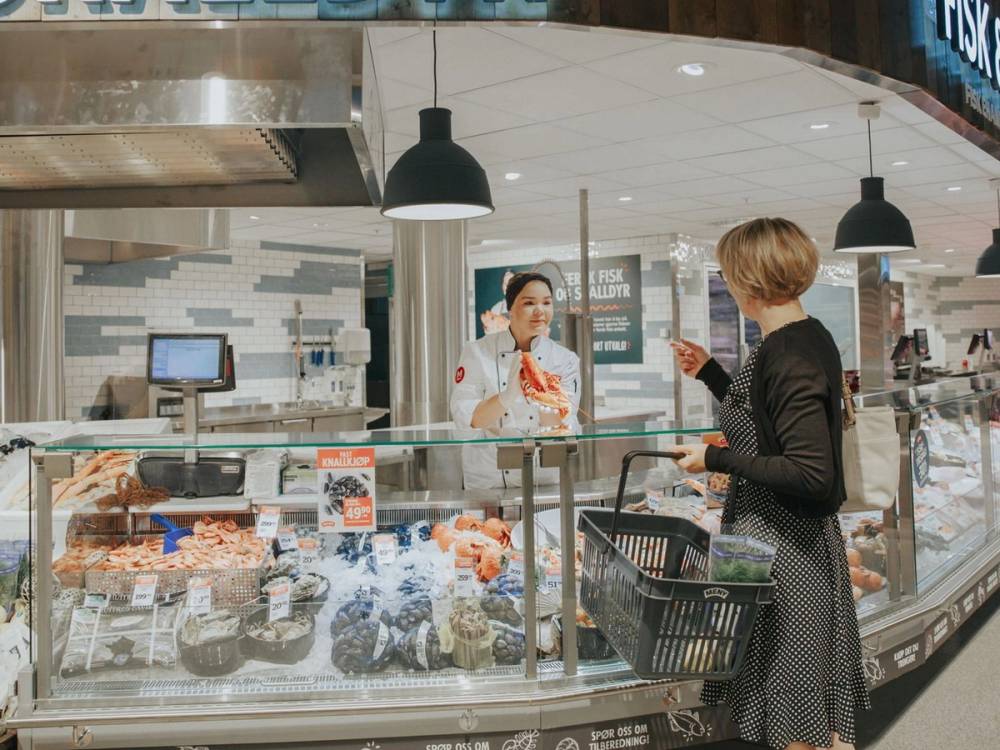 En kunde handler i ferskvaredisken på en matbutikk, med en ansatt som hjelper til.