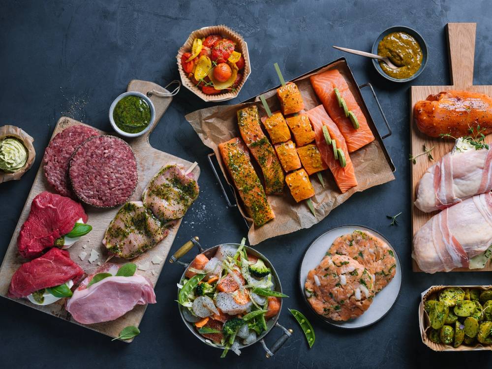 Et utvalg av ulike grillmatvarer som kjøtt, fisk, grønnsaker og sauser på et bord.