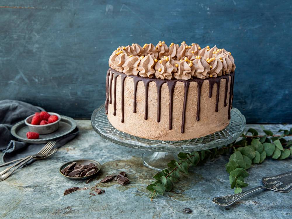 En oreo dripcake med bringebær på toppen, dekorert med sjokoladedrips og krem, plassert på et fat med noen bringebær og sjokoladebiter rundt.