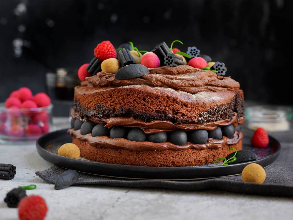 En sjokoladekake med lakrisdekorasjoner og frukt på toppen, ser ut til å være en kake med lag og fyll.