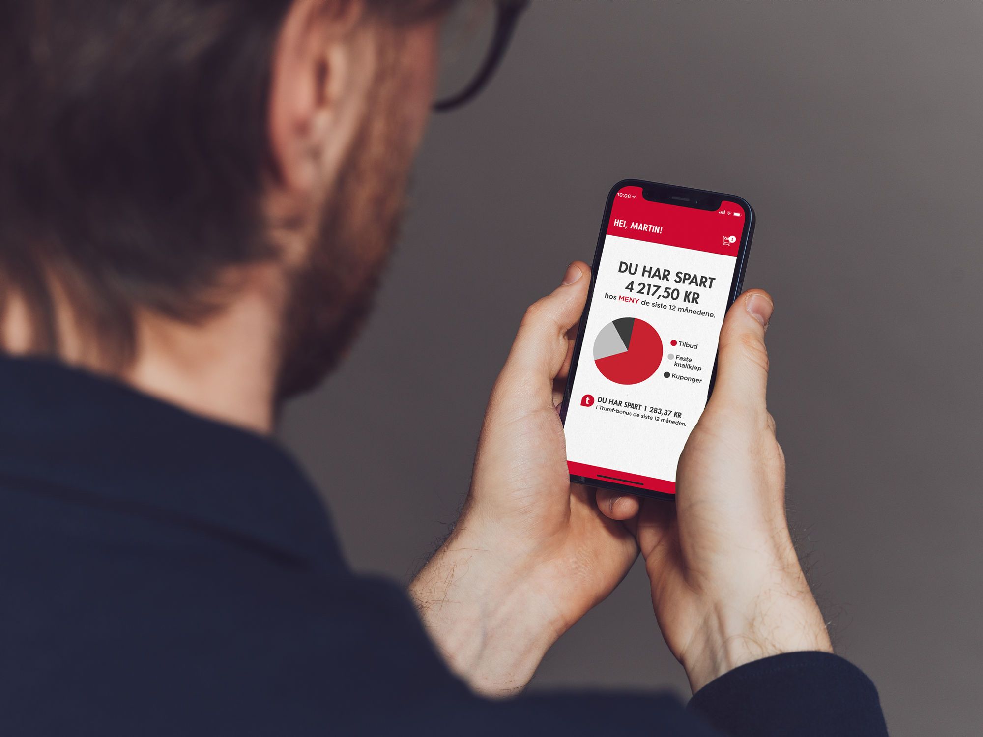 En person ser på en mobilskjerm som viser en oversikt over besparelser hos Meny, med en graf og tekst om sparing.