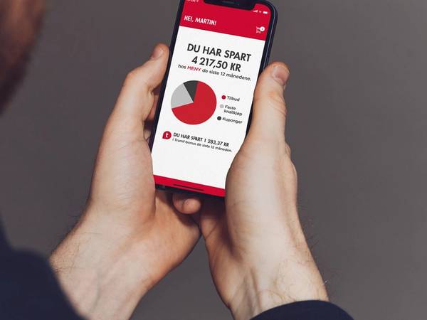 En person ser på en mobilskjerm som viser en oversikt over besparelser hos Meny, med en graf og tekst om sparing.