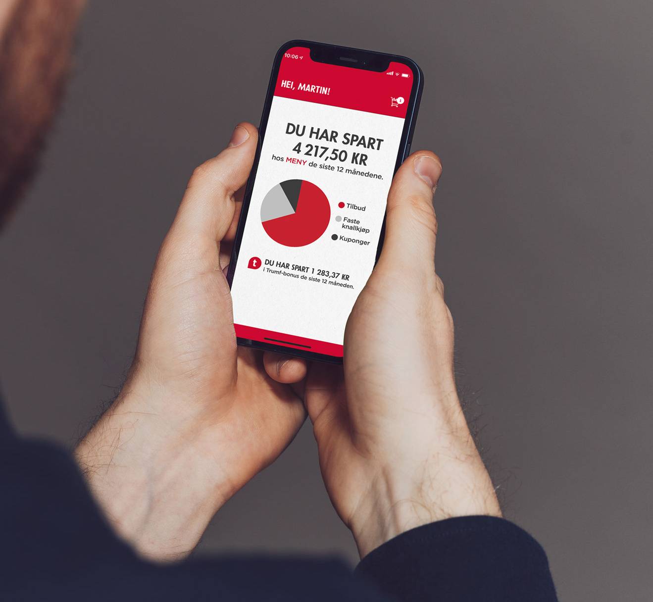 En person ser på en mobilskjerm som viser en oversikt over besparelser hos Meny, med en graf og tekst om sparing.