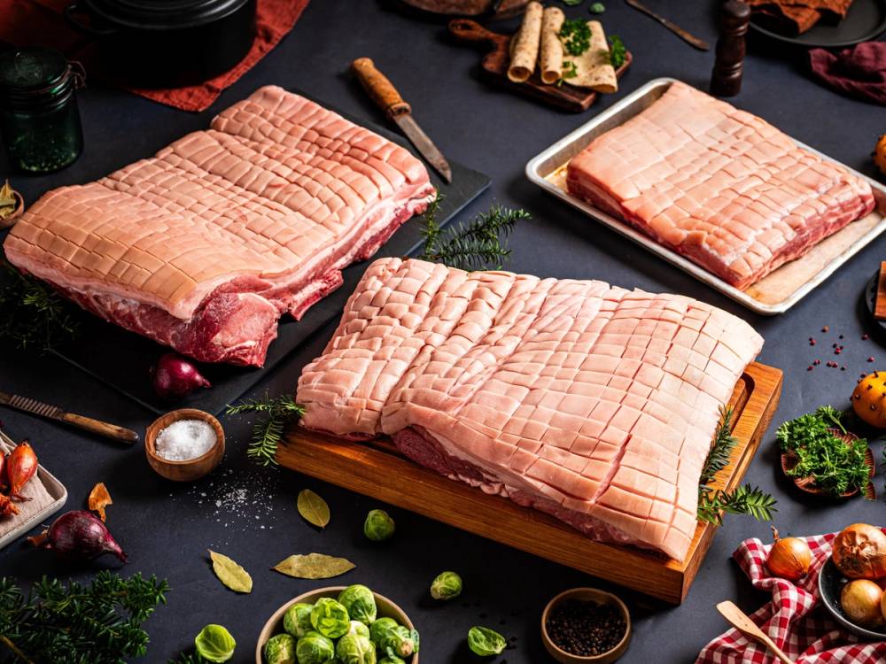 Ulike stykker av ribbe lagt ut på bord med julepynt og krydder rundt, klar for tilberedning.